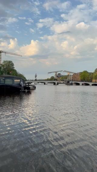 A calm river scene with a boat and bridge under a cloudy sky